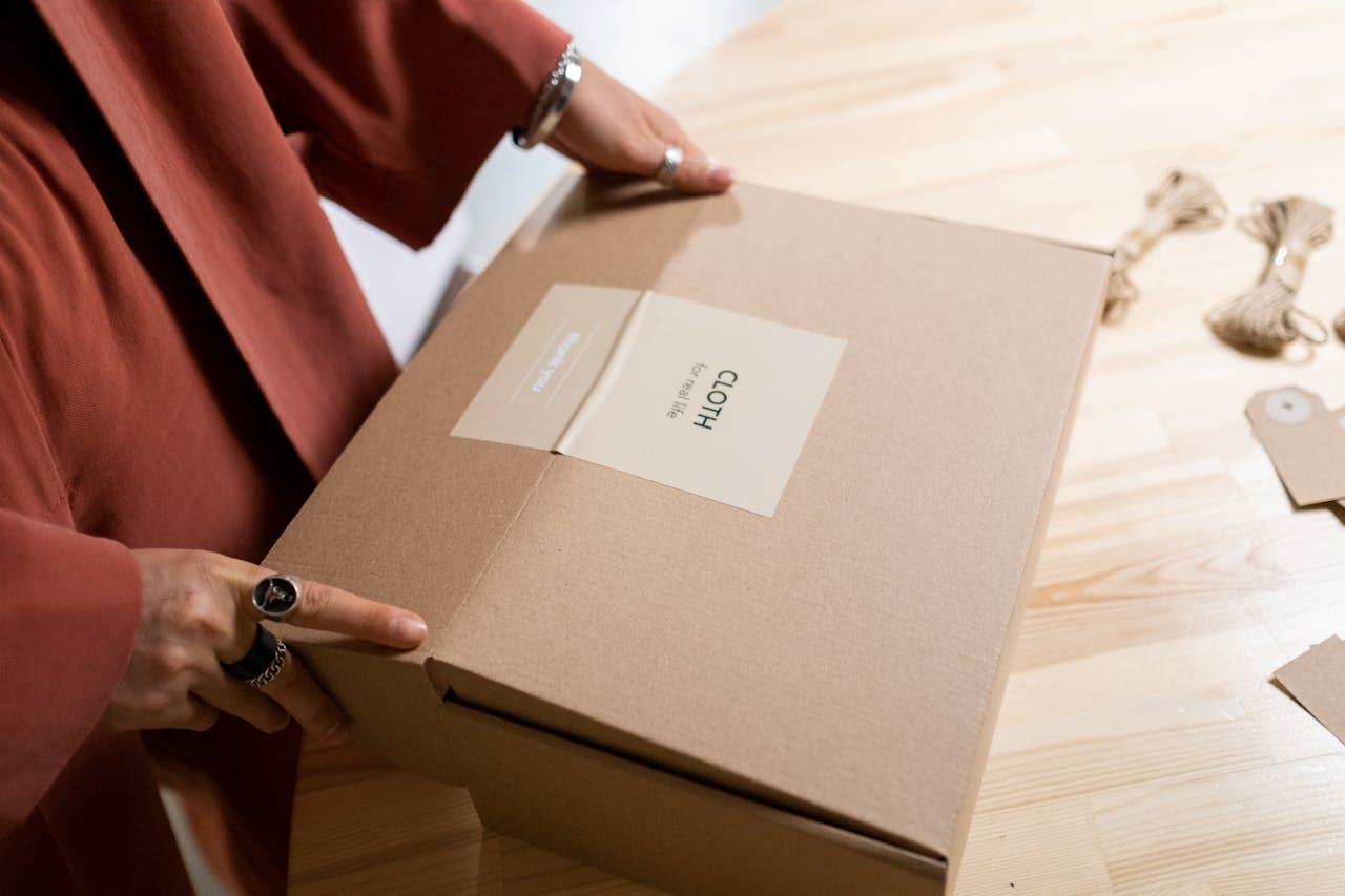 services-01 Close-up of a woman packing a cardboard box on a wooden table indoors.